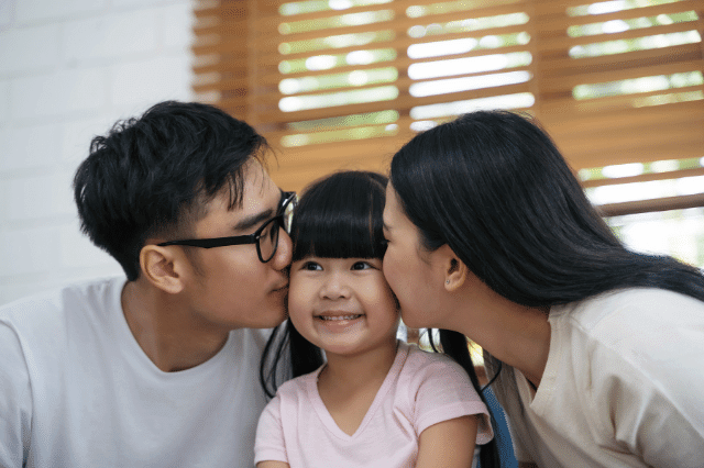 A father and mother is kissing their daughter lovingly.