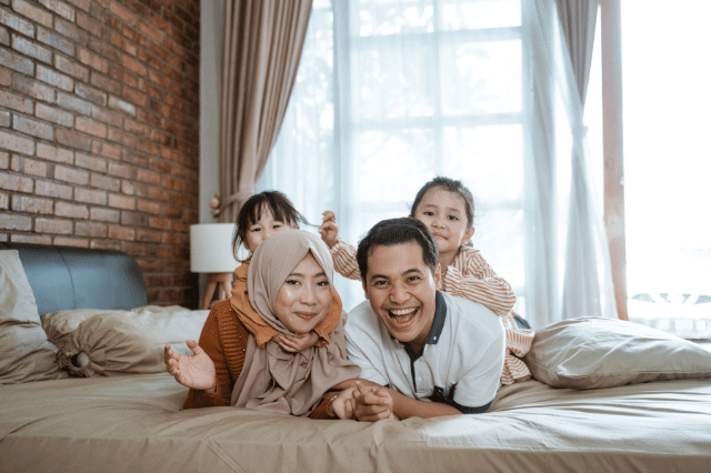 A family of four is sitting on the bed happily.