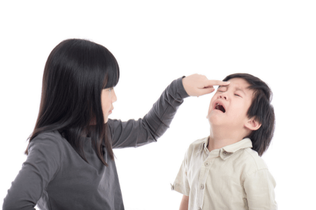 An elder sister is pointing at her crying little brother.