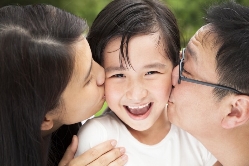 parents kissing child on cheek