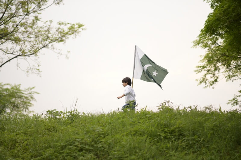 Patriotic young boy running with a Pakistan flag