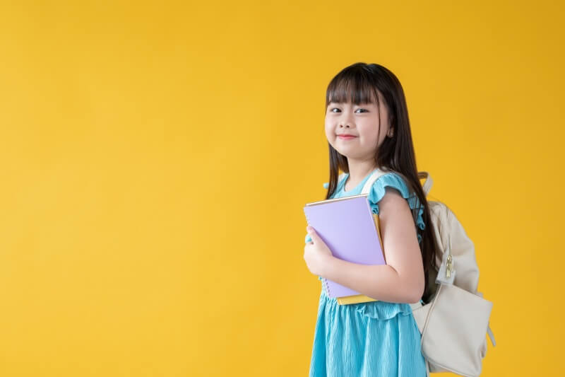 young girl carrying school bag in yellow isolated background