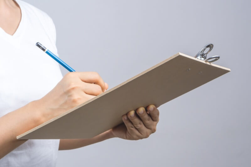 Woman hand holding wooden clipboard and a pencil on grey background